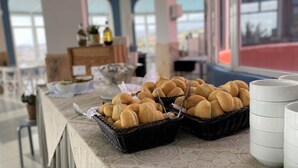 A buffet table with baskets of bread and white plates, a bottle, and a buffet setup in a room with large windows and a view. - Laguna Park 2 (Adeje)