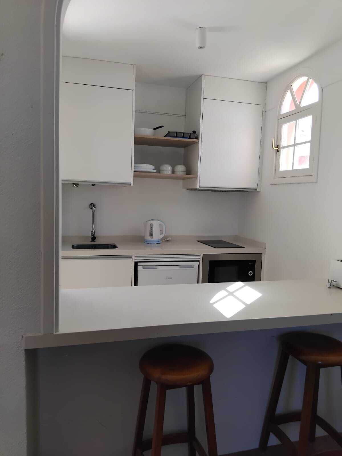 Una cucina compatta con mobili bianchi, lavastoviglie integrata, bollitore e una finestra vista.