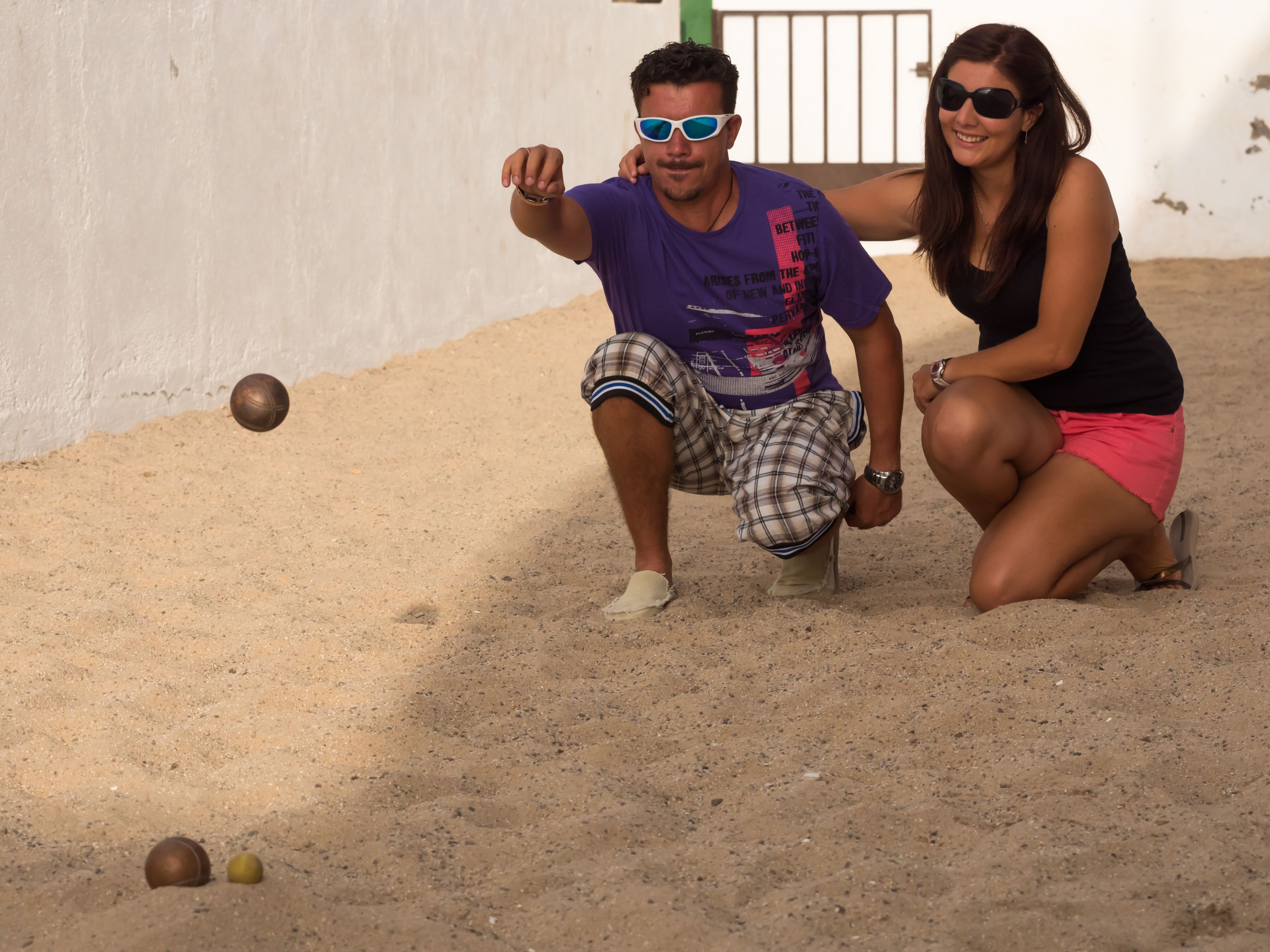 Un hombre y una mujer jugando a un juego en un suelo arenoso con una pelota.