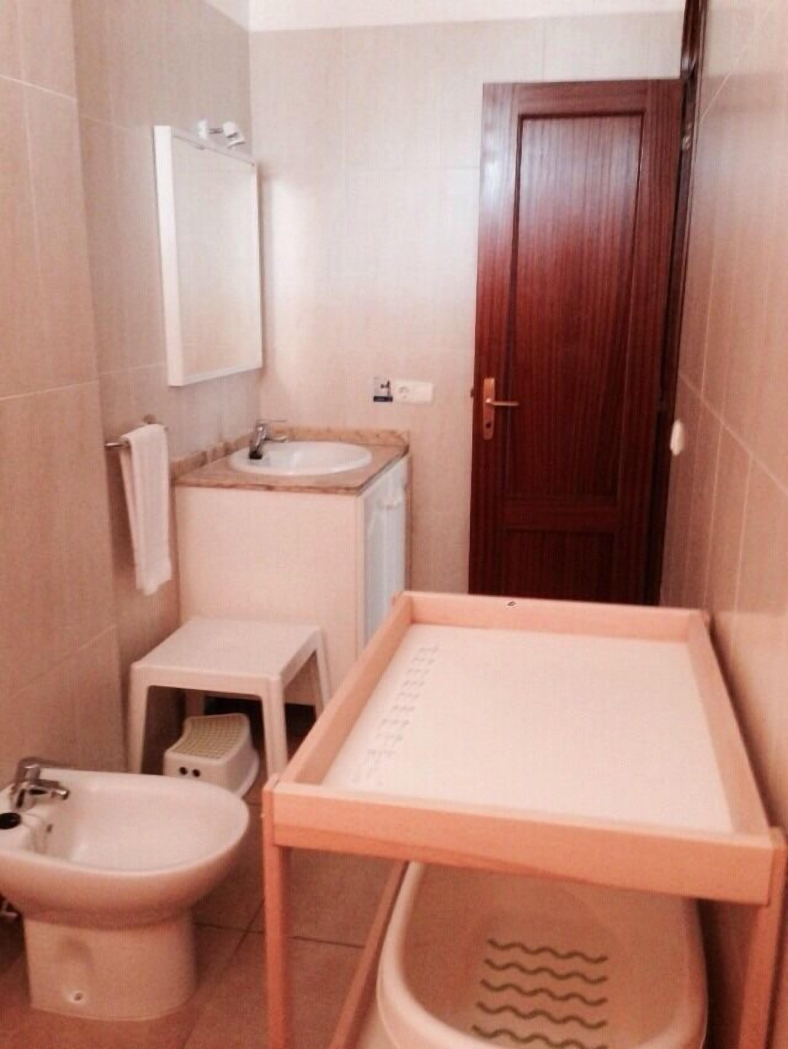 A small bathroom with a toilet, bidet, sink, and a wooden cabinet.