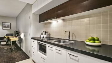 A modern kitchen with a black countertop, stainless steel sink, and a bowl of green apples.