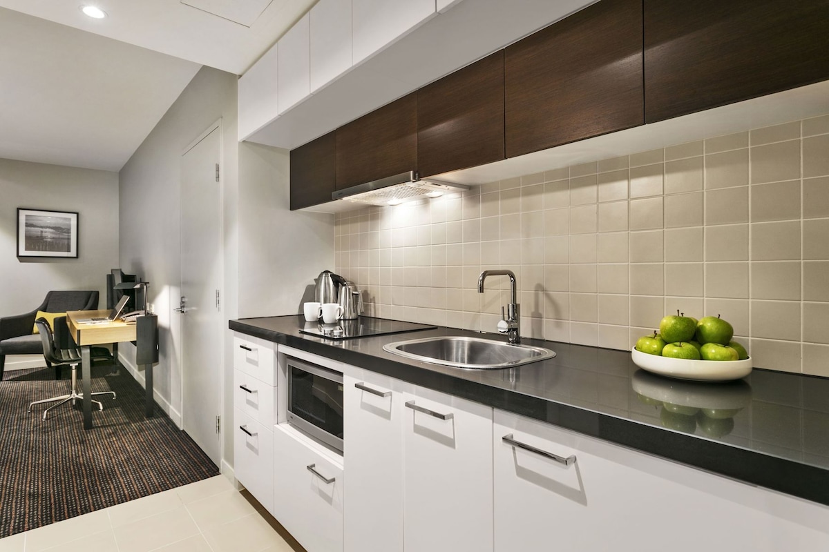 A modern kitchen with a sink, stove, and a bowl of green apples on the counter.