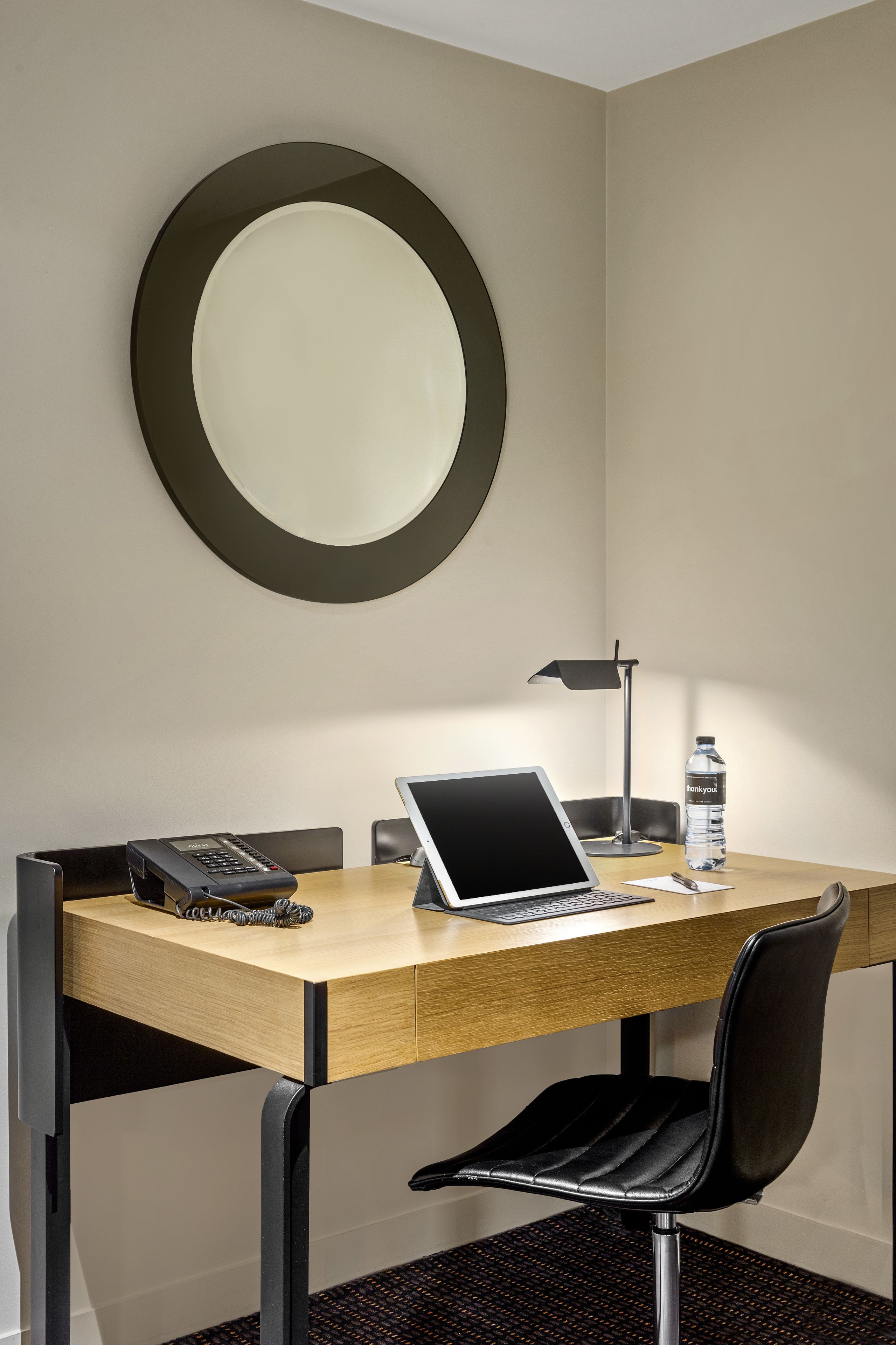 Une chambre d’hôtel avec un bureau en bois, un ordinateur portable, un téléphone, une bouteille d’eau et une chaise.