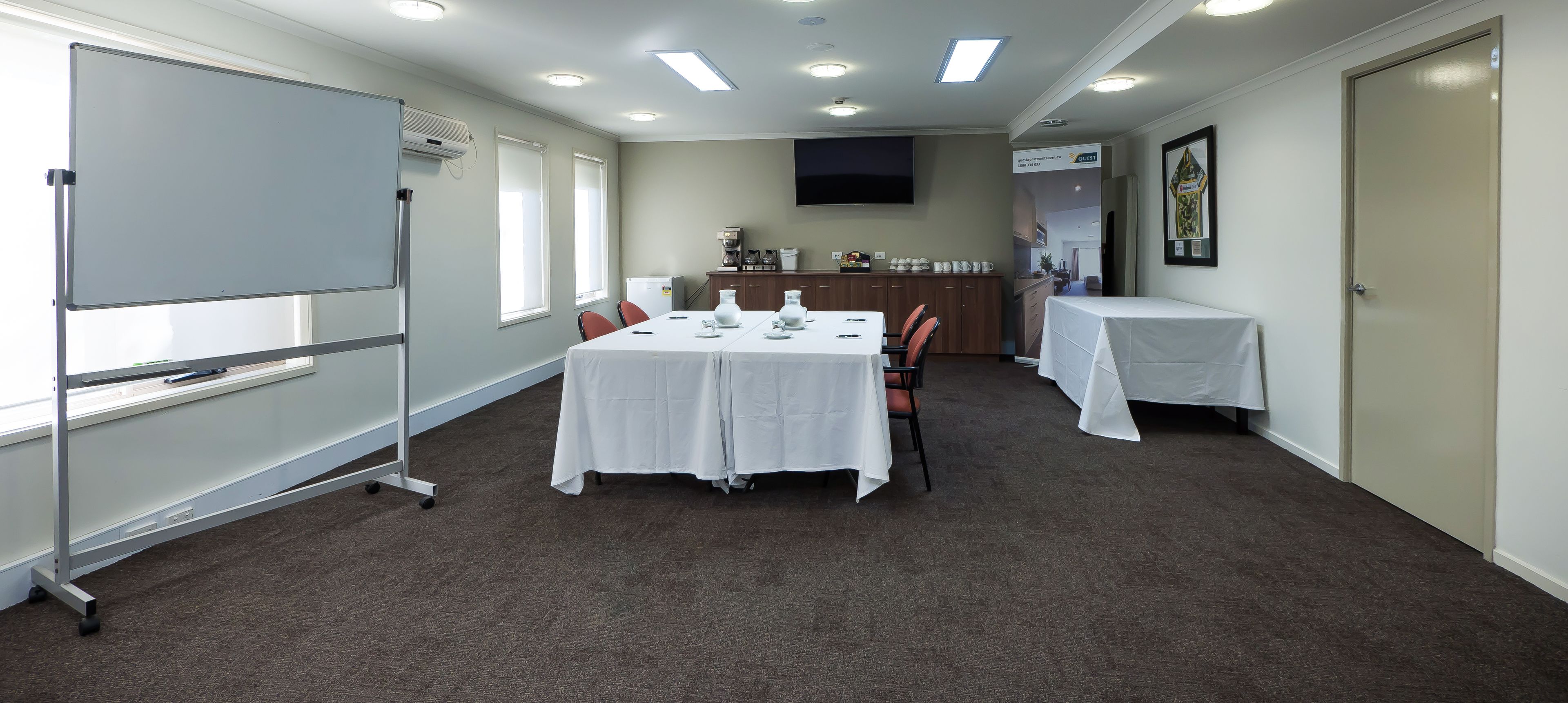 A conference room with a white table, chairs, a whiteboard, and a TV on the wall.