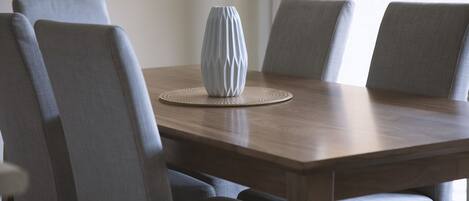 A dining table with four grey upholstered chairs, a white vase, and a woven placemat.