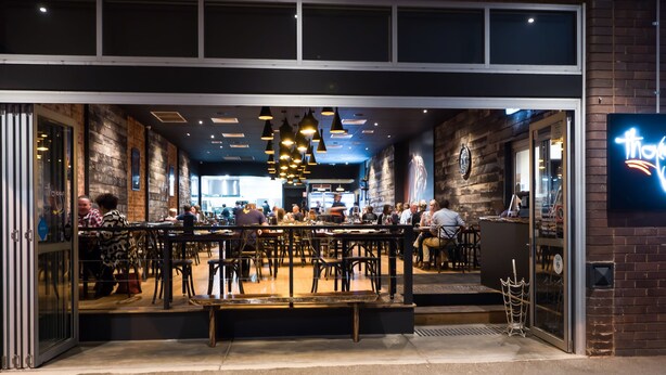 Un restaurant à l’extérieur en briques, doté de grandes fenêtres et de luminaires suspendus.