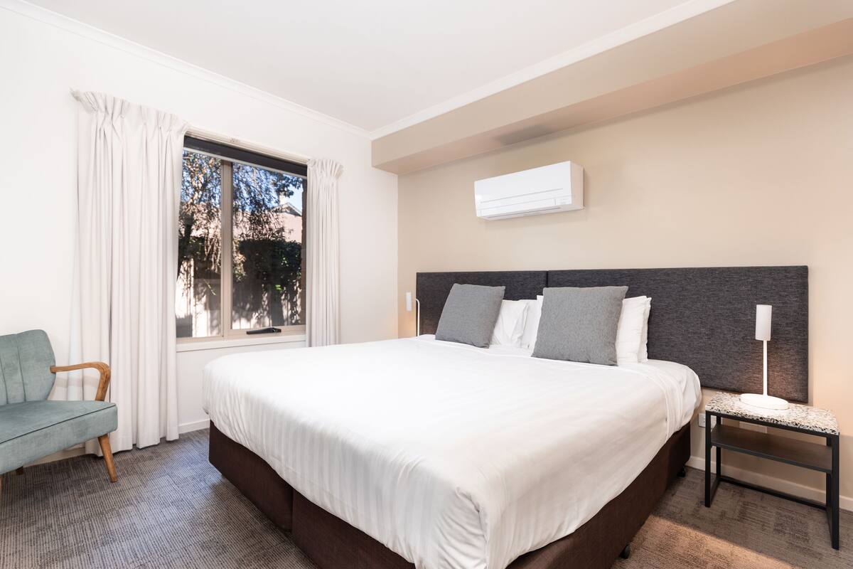 Een hotelkamer met een groot bed, een stoel, een nachtkastje en een raam met gordijnen.