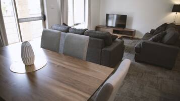 Un salon moderne avec une table à manger en bois, des canapés gris, un téléviseur à écran plat et une lampe.