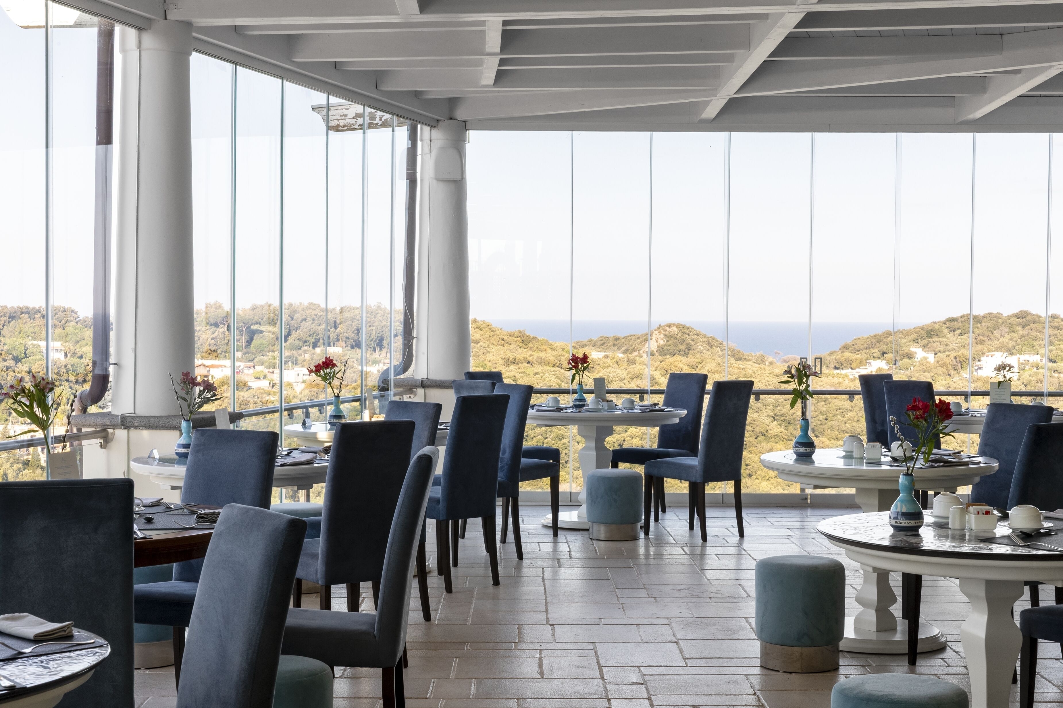 Een restaurant met terras, grote ramen en uitzicht op de heuvels.