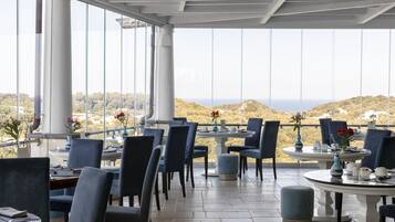 Een restaurant met terras, grote ramen en uitzicht op de heuvels.
