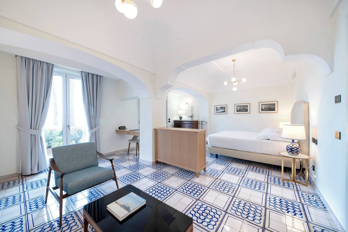 Ein Hotelzimmer mit einem Bett, einem Schreibtisch, einem Stuhl, einem Couchtisch und einem gemusterten Boden.