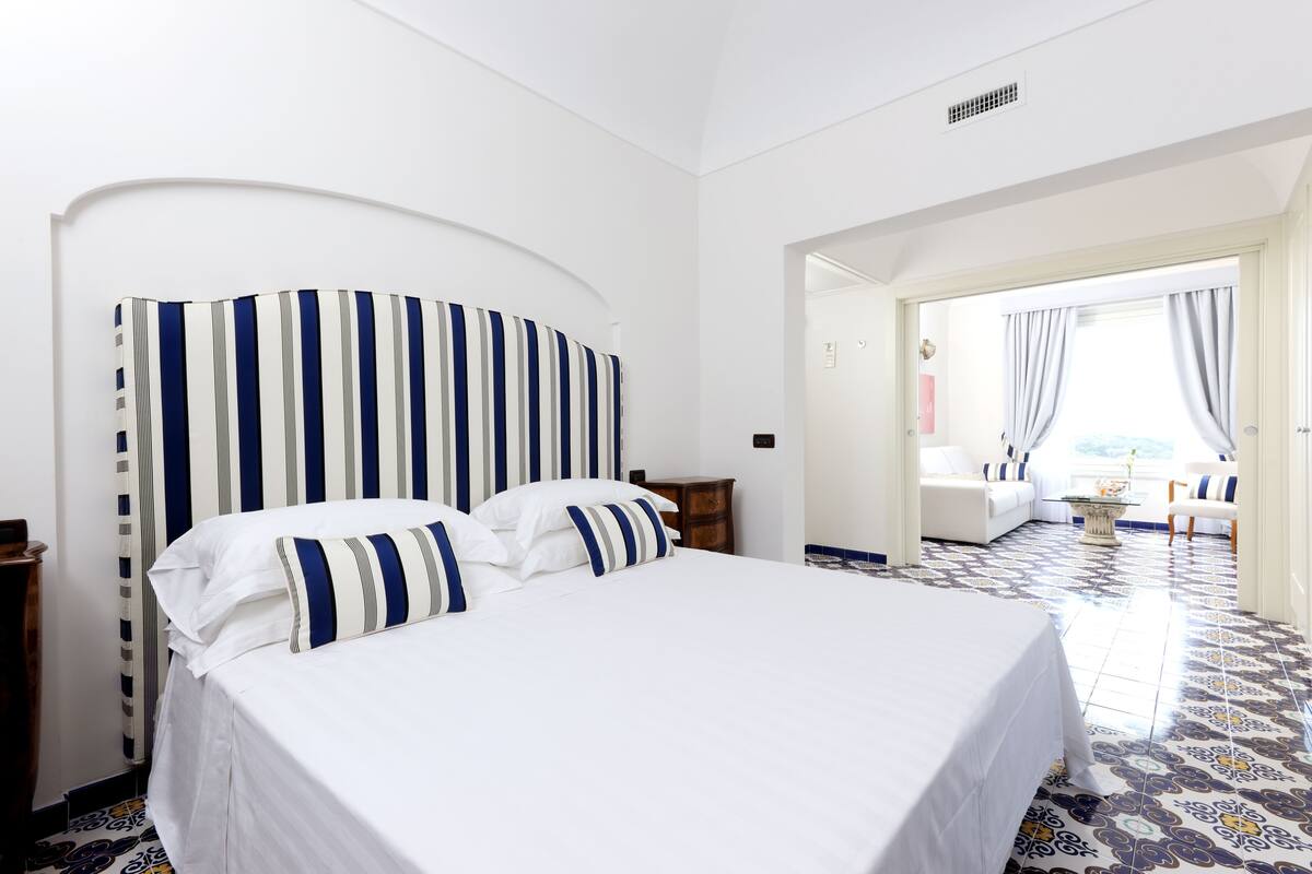 Ein Hotelzimmer mit einem großen Bett, einem gebogenen Kopfteil, einem Holznachttisch und einem gestreiften Boden.