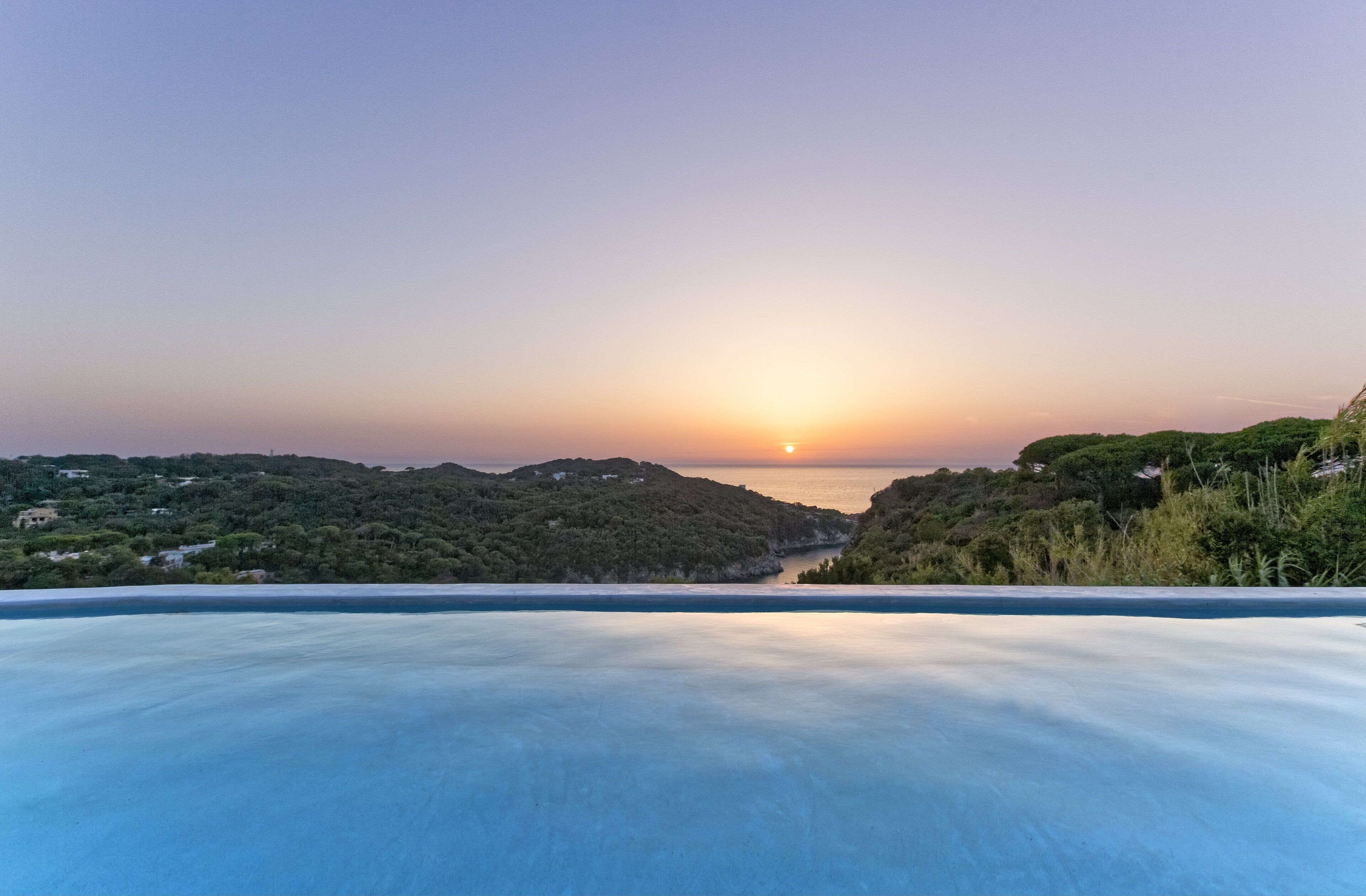 Panoramica di un paesaggio costiero con cielo sereno, tramonto e un tratto d'acqua.