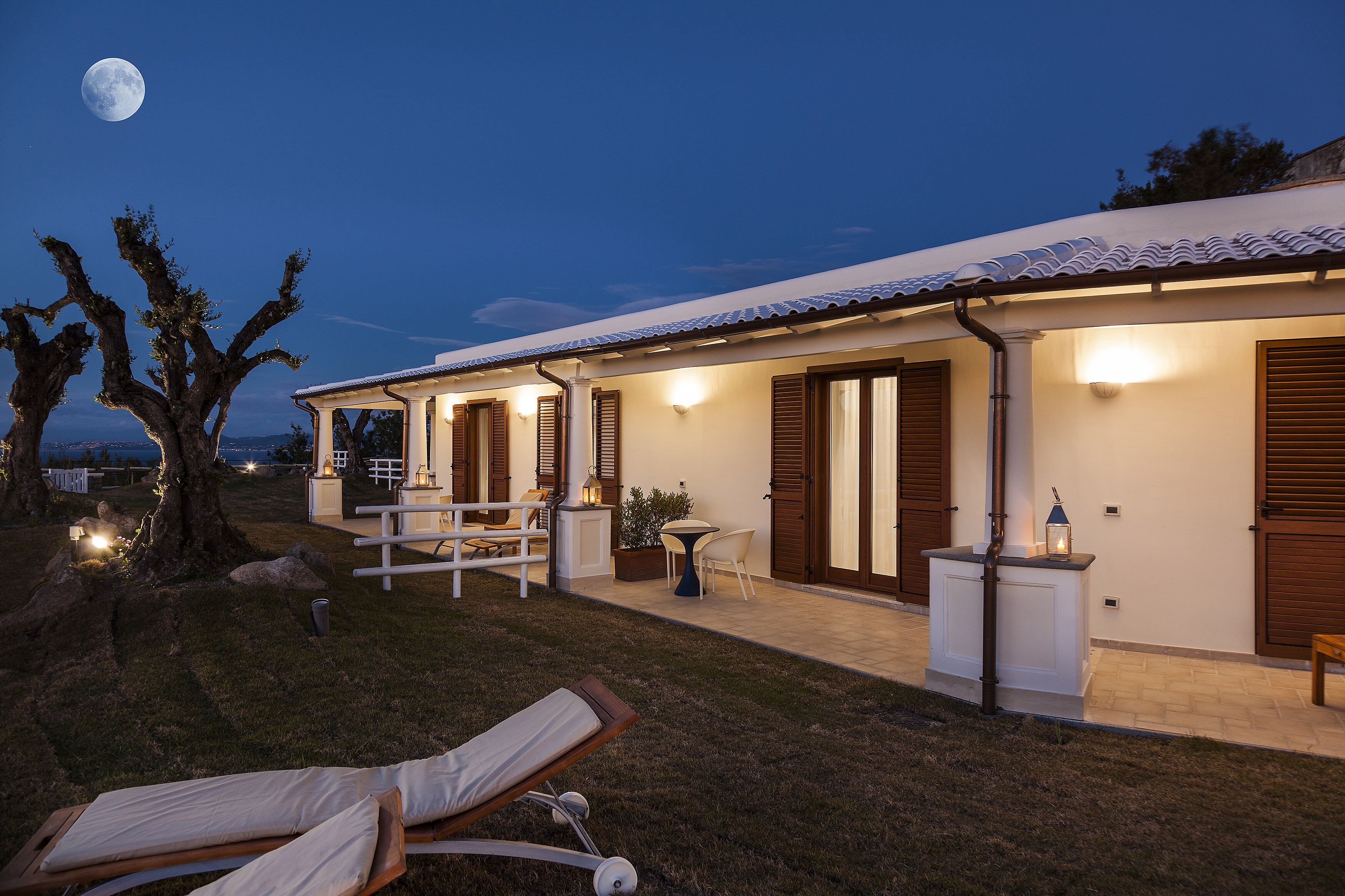 Une maison moderne avec un patio, un fauteuil de relaxation et la lune dans le ciel.