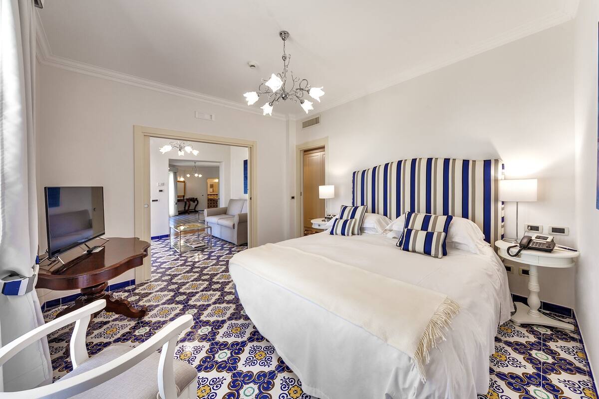 Ein Hotelzimmer mit einem großen Bett, einem Schreibtisch mit Fernseher, Telefon und Lampe.