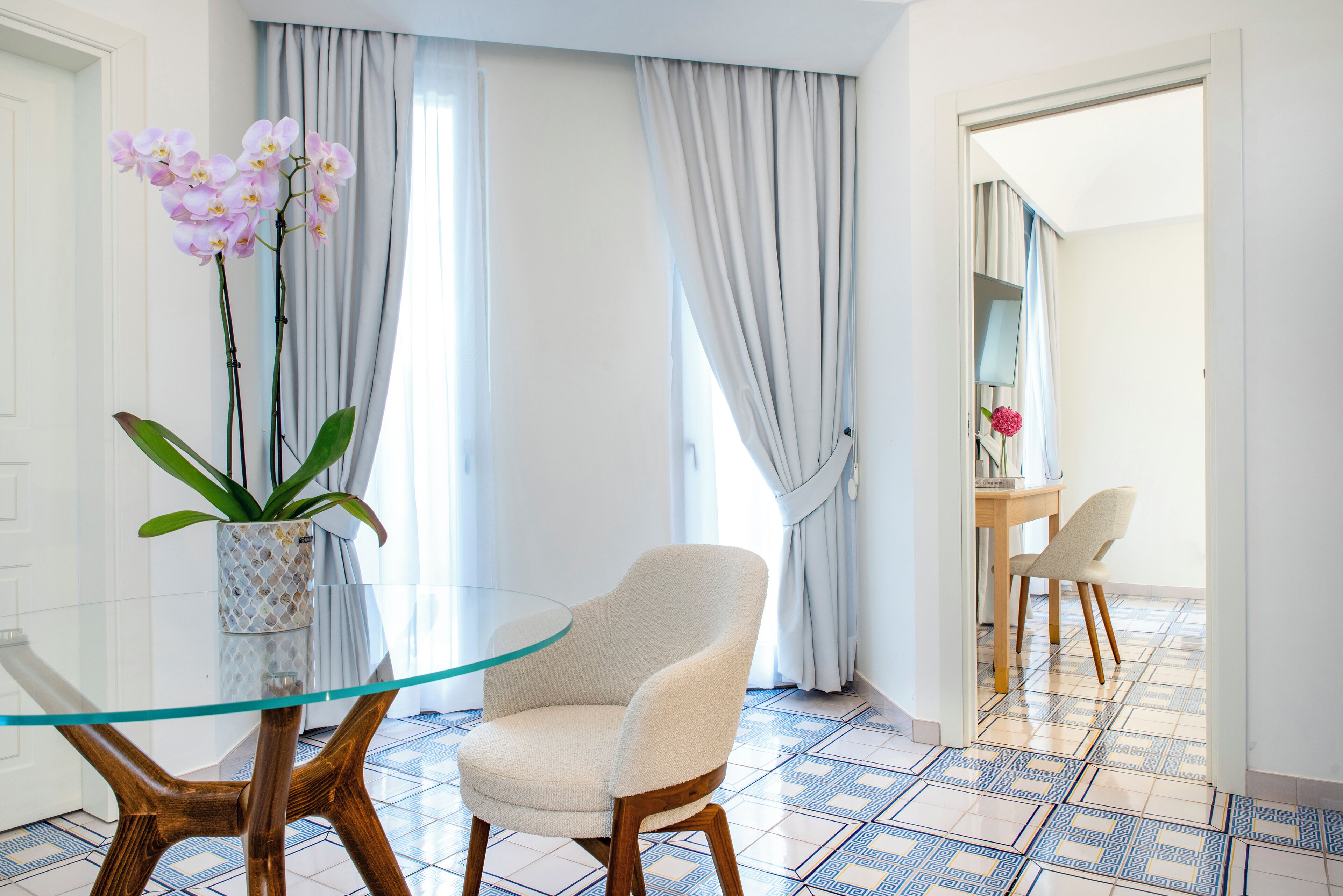 A modern room with a glass table, a white armchair, and a potted orchid.
