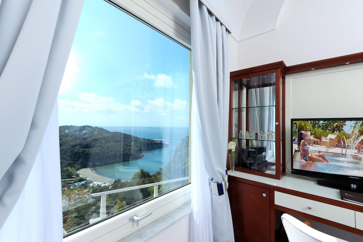 Ein Zimmer mit großem Fenster und Blick auf eine Küstenlandschaft, einem Fernseher und einer Holzschrank.