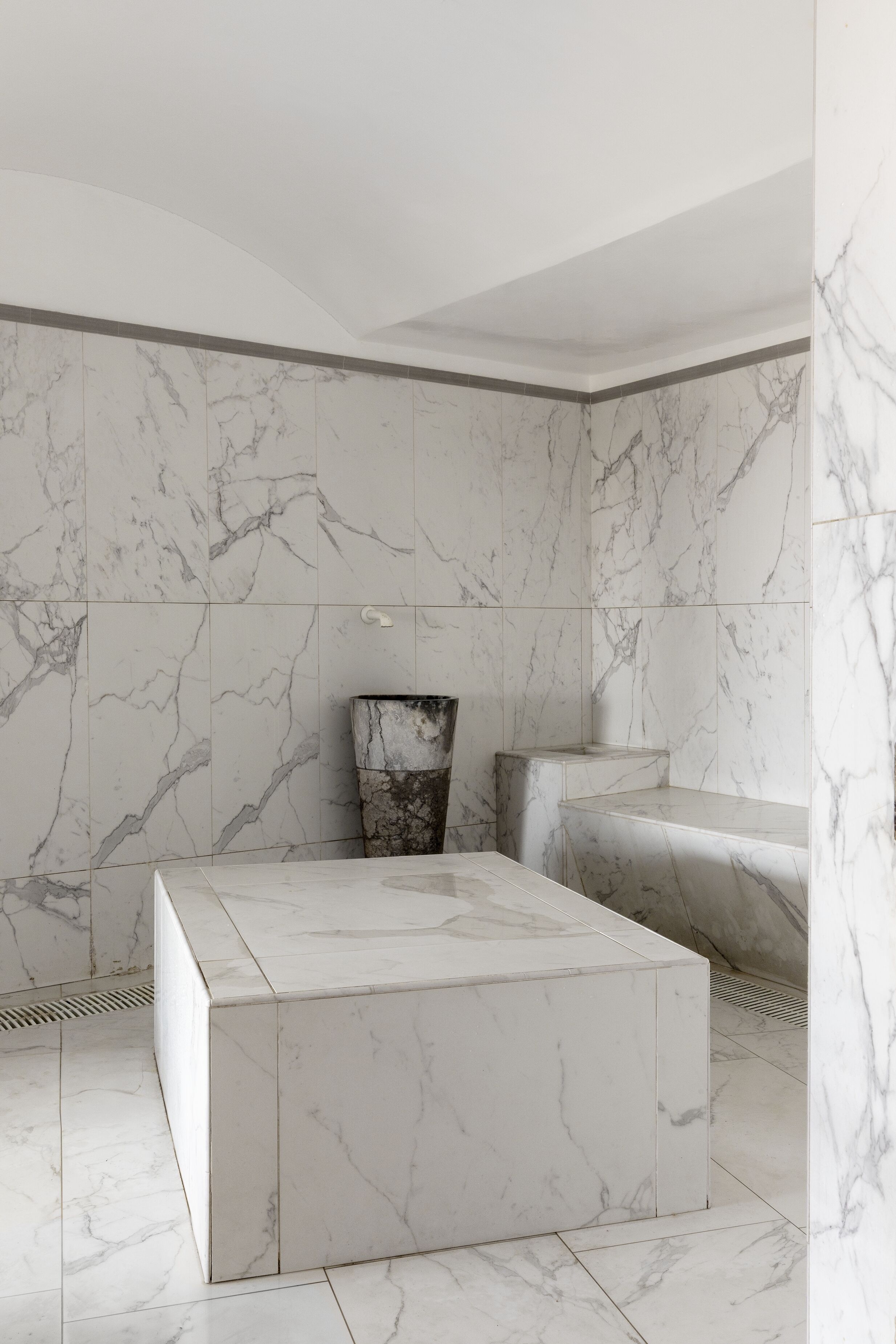 Une salle de bain moderne avec des murs en marbre et une colonne centrale.