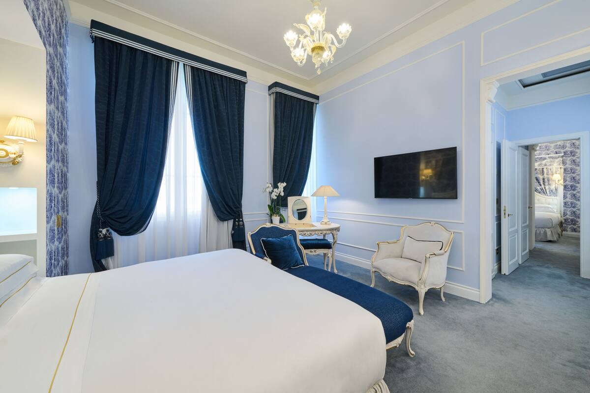 A hotel room with a large bed, a desk with a lamp, a chair, and a television on the wall.