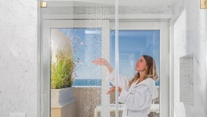A person in a white robe standing in a shower with water spraying out.