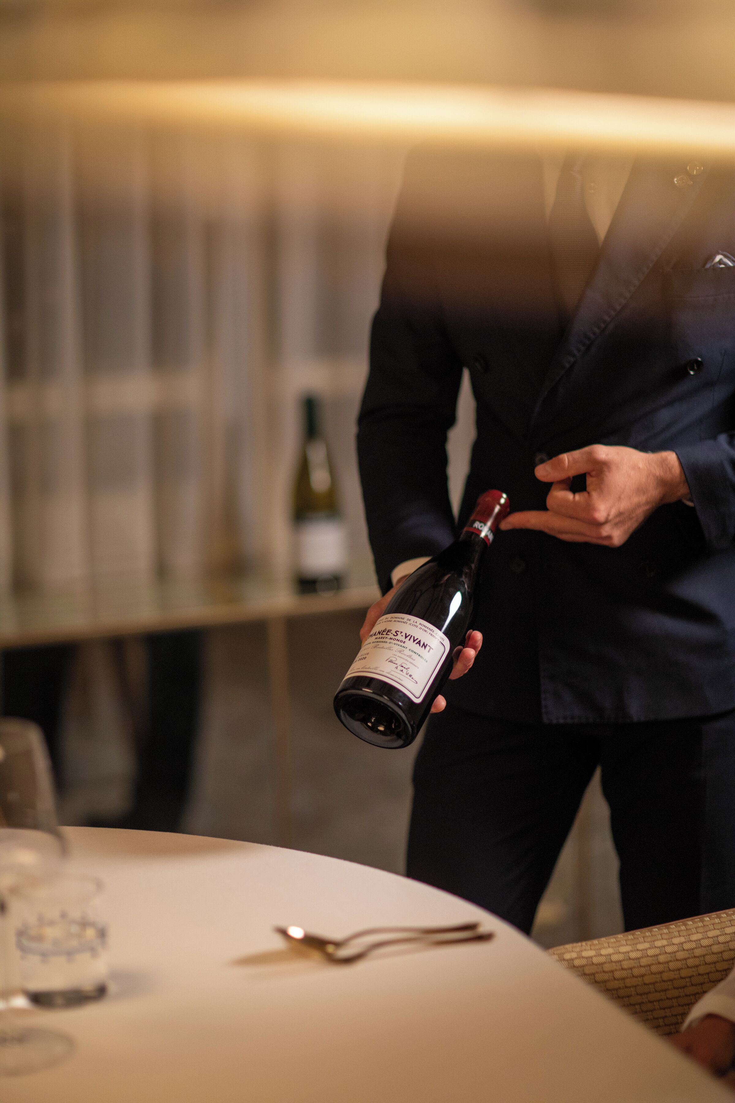 A person holding a wine bottle in a room with a table and chairs.