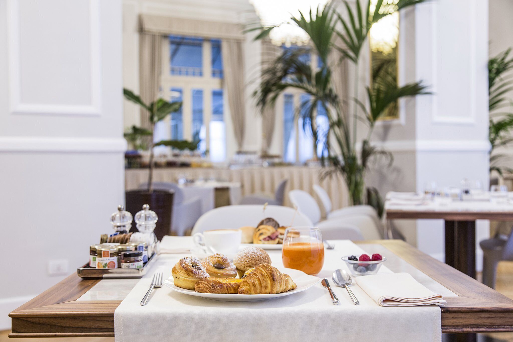 A breakfast table with pastries, a fruit bowl, and a glass of orange juice.