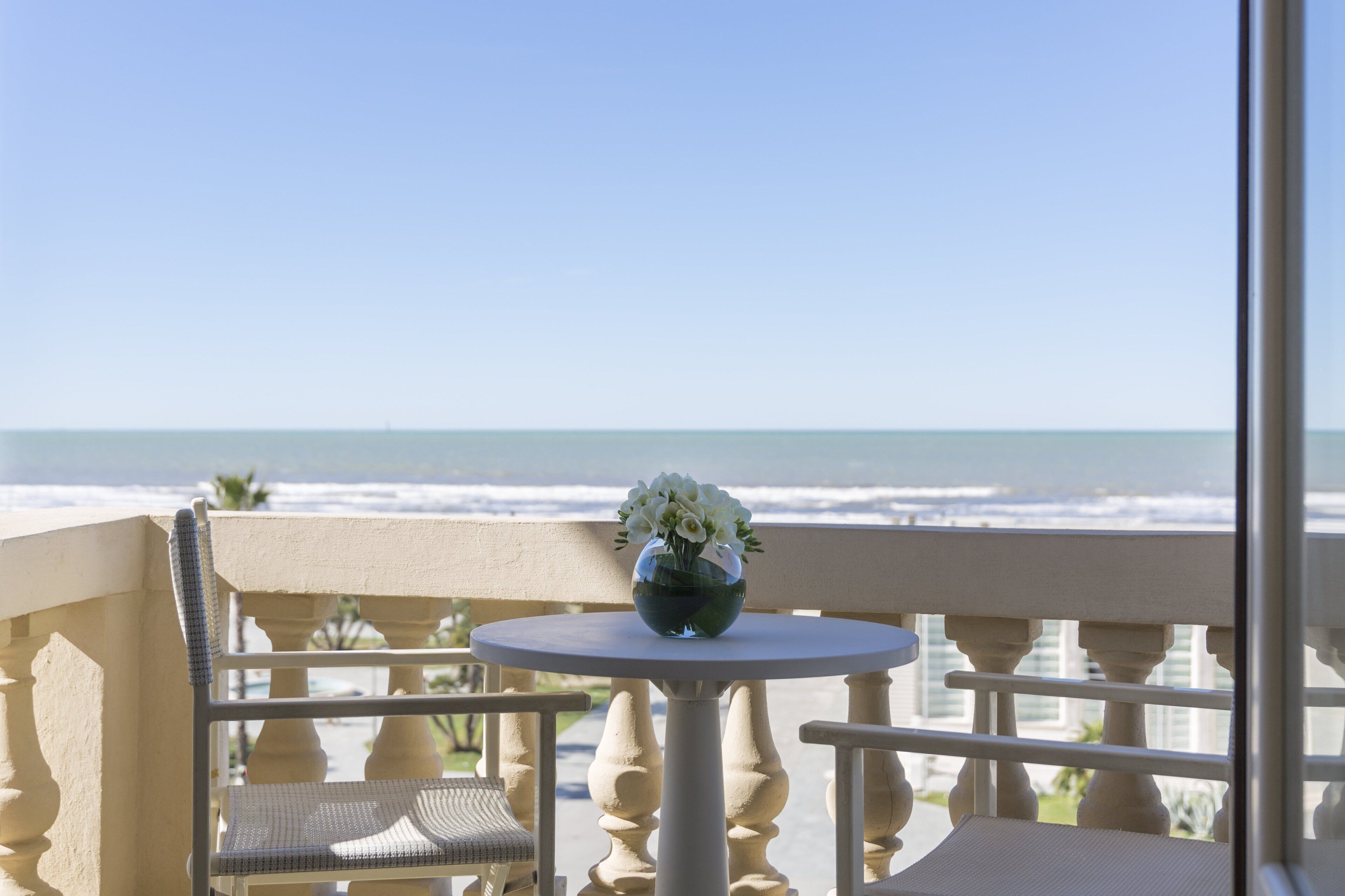 A balcony with a table and chairs, overlooking the ocean.