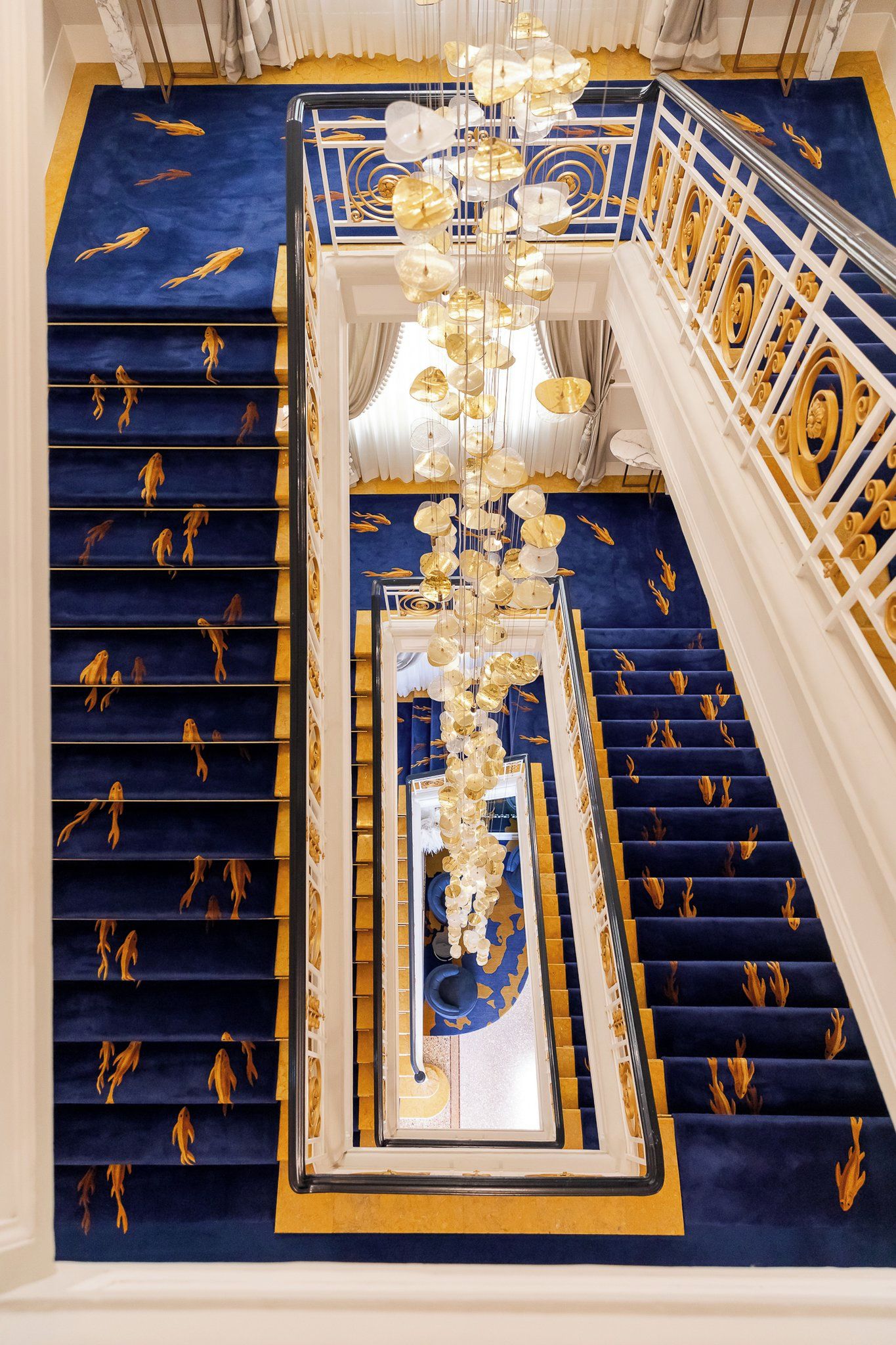 Una imponente escalera con alfombra azul y detalles dorados, que conduce a un balcón con vistas.