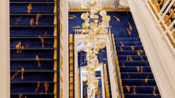 Una imponente escalera con alfombra azul y detalles dorados, que conduce a un balcón con vistas.