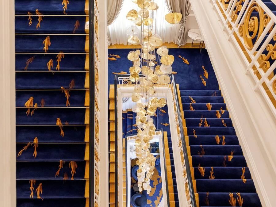 A grand staircase with blue carpet and gold accents, leading to a balcony with a view.