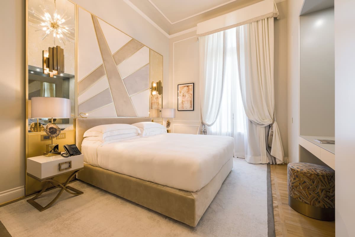 A modern hotel room with a large bed, bedside tables, a mirror, and a decorative light fixture.
