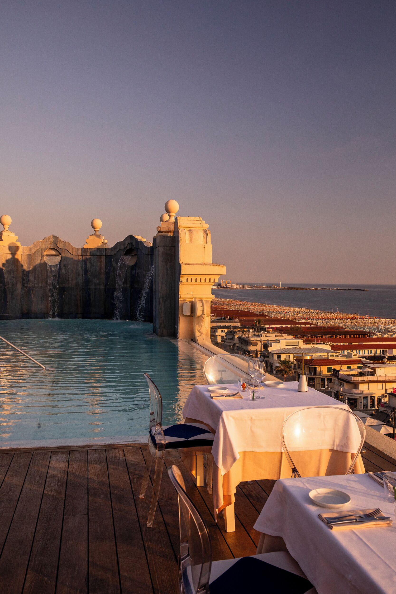 Una piscina sul tetto con vista sulla spiaggia e sullo skyline cittadino, circondata da tavoli e sedie.