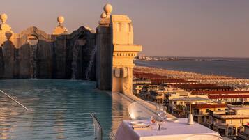Una piscina sul tetto con vista sulla spiaggia e sullo skyline cittadino, circondata da tavoli e sedie.