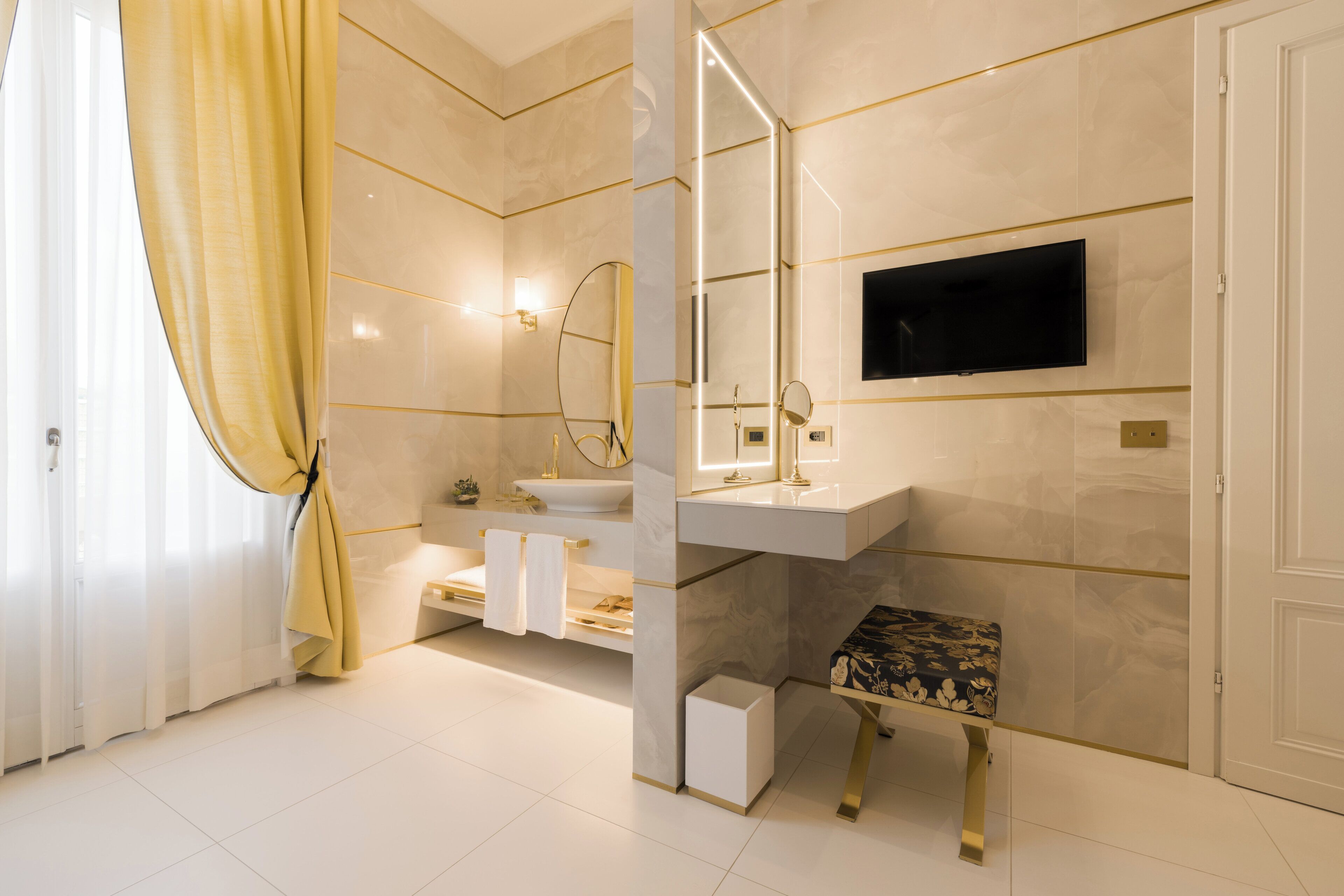 Une salle de bain moderne équipée d’un meuble-lavabo, d’un évier, d’un miroir, d’un banc et d’un téléviseur fixé au mur.