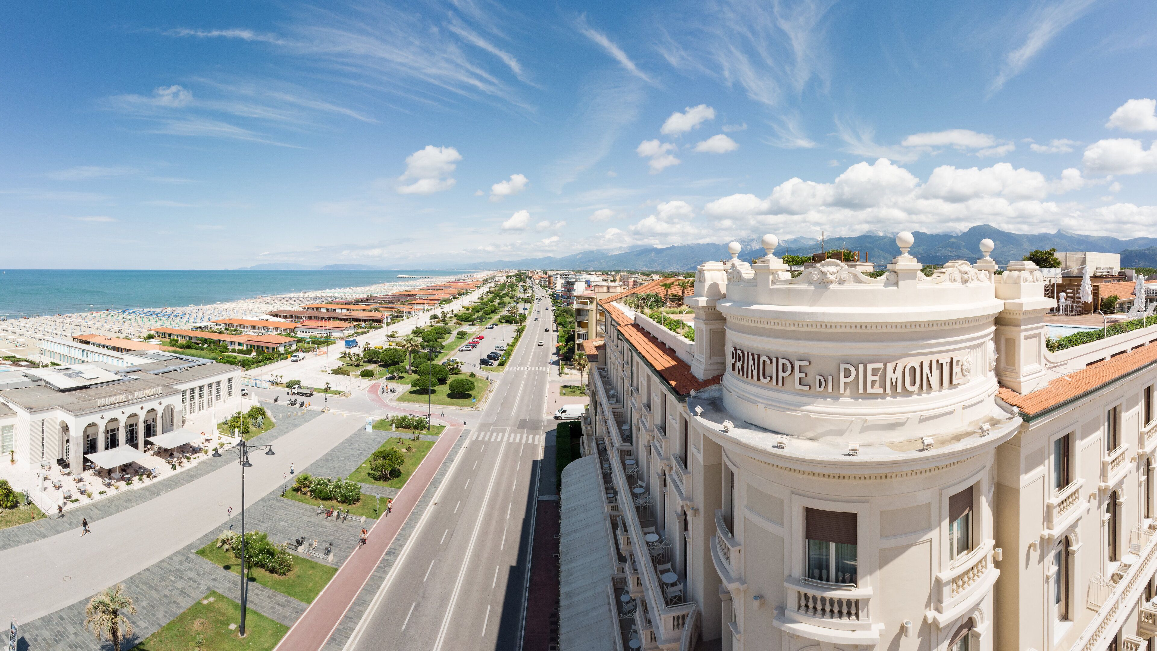 A hotel with a prominent "PRINCIPE DI PIEMONTE" sign, a wide road, and a beach in the background.