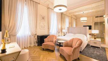 Quarto de hotel com cama, duas poltronas, escrivaninha, abajur e espelho.