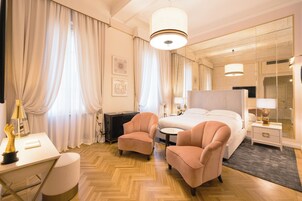 Quarto de hotel com cama, duas poltronas, escrivaninha, abajur e espelho.