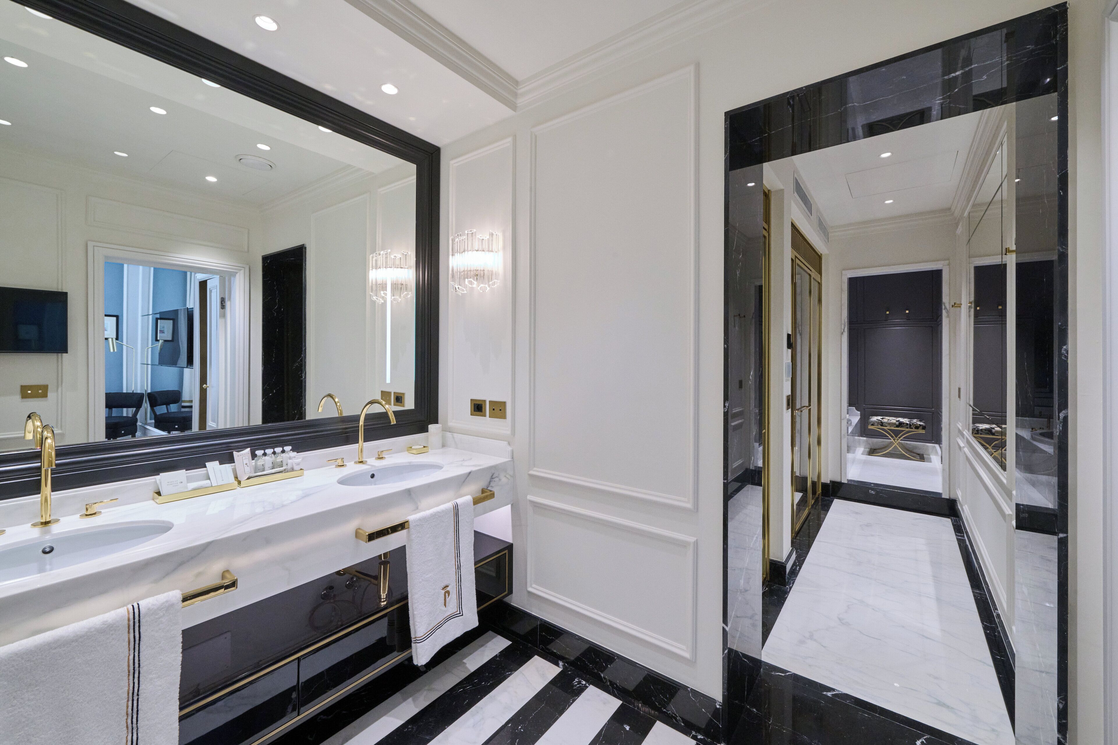 A luxurious bathroom with a double sink vanity, a large mirror, and a black and white marble floor.