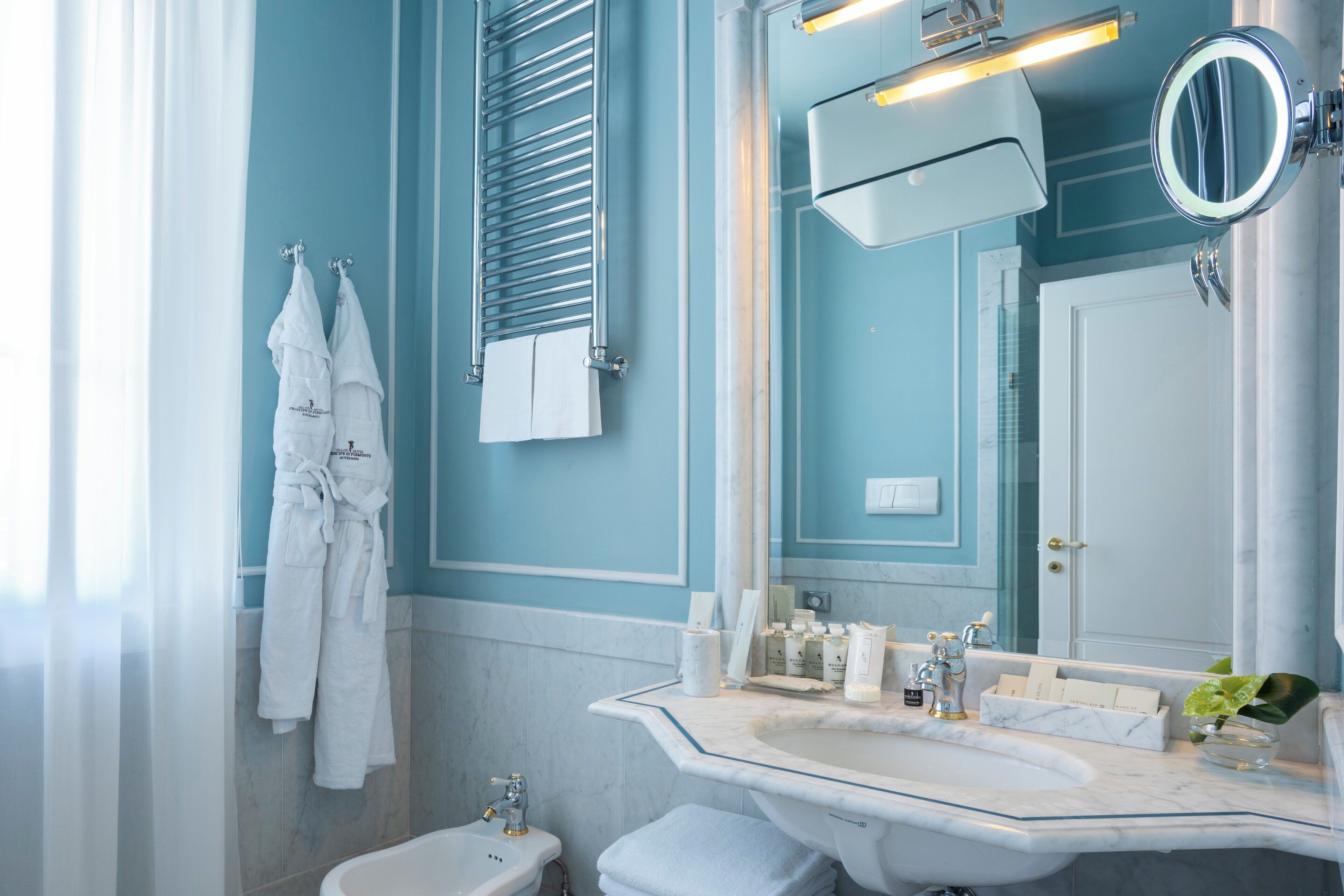 Un baño con lavamanos blanco, un espejo y un perchero con toallas blancas.