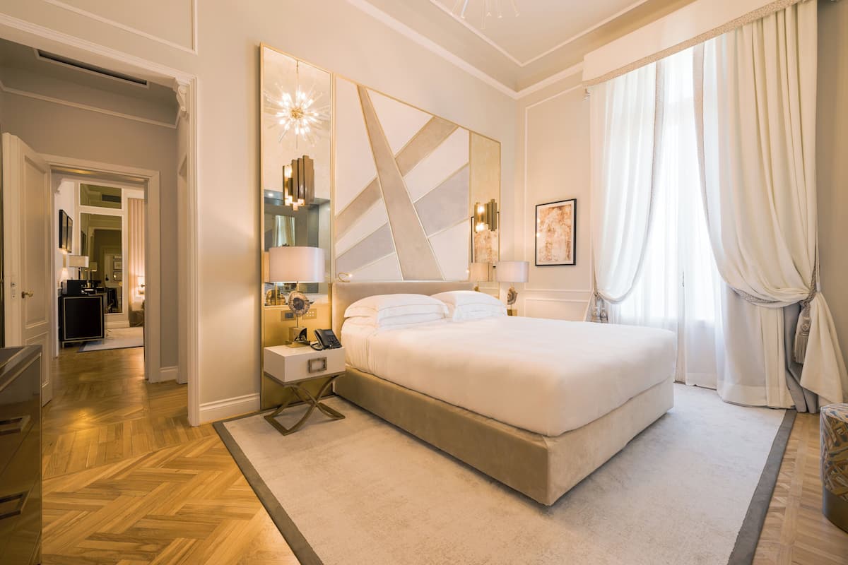 A spacious bedroom with a large bed, a bedside table with a lamp, a mirror, and a decorative wall piece.