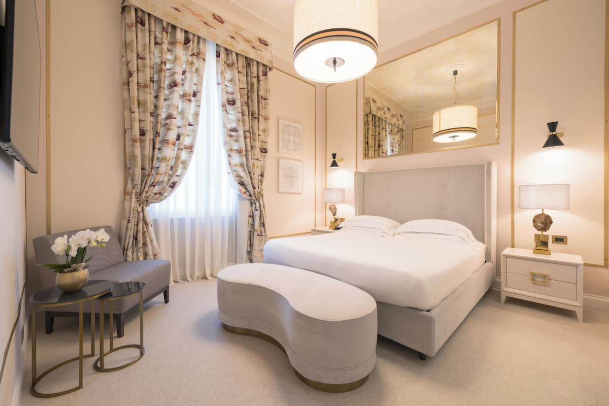 A modern bedroom with a large bed, a bedside table, a nightstand, a sofa, and a small table with a lamp.