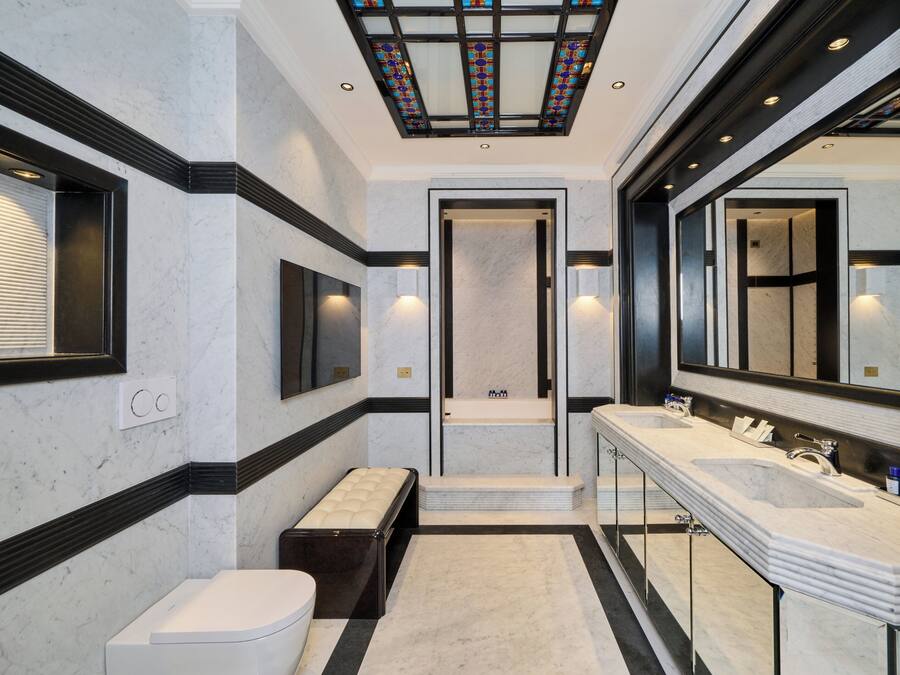 A modern bathroom with a large mirror, two sinks, a bench, and a shower area.