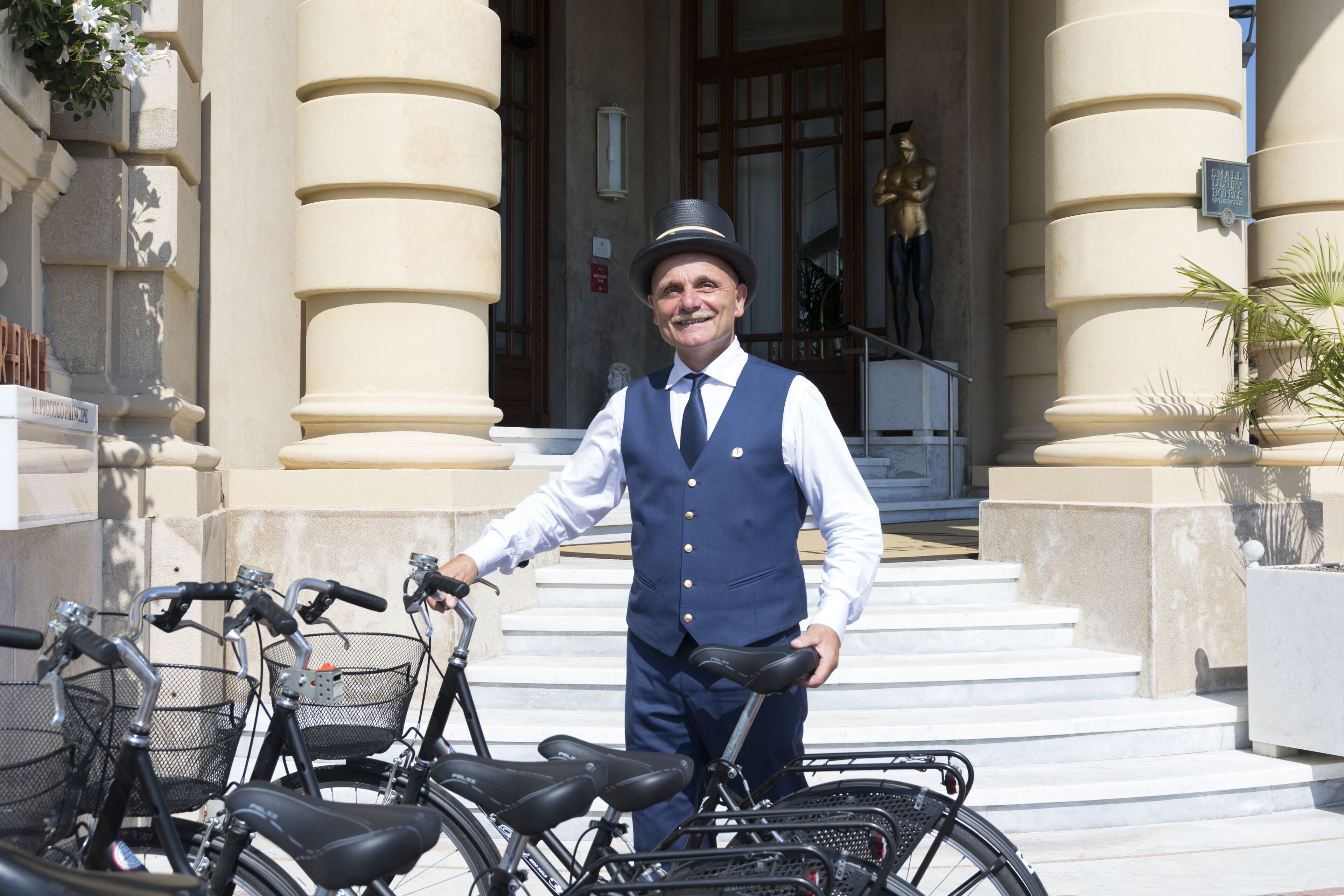 Un homme se tient à côté de vélos devant un bâtiment doté de grandes colonnes et d’un escalier.