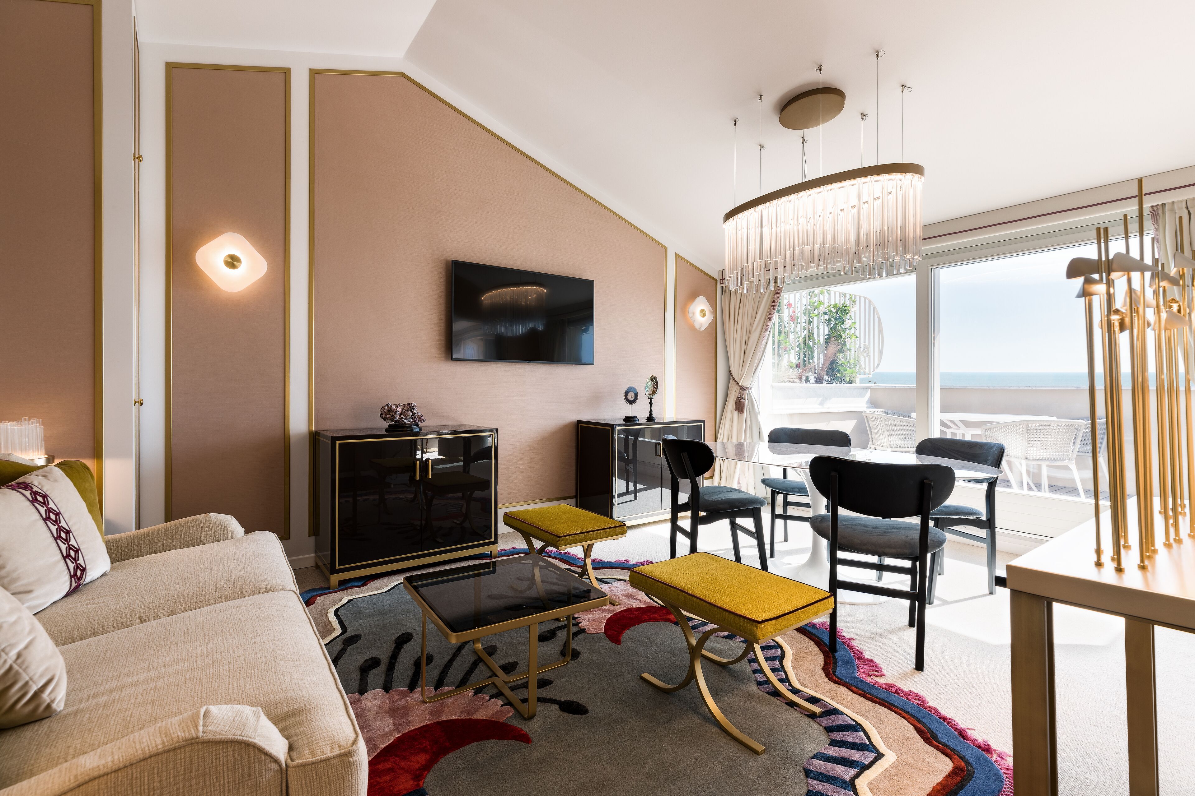 Una sala de estar moderna con sofá, mesa de centro y sillas, un televisor de pantalla plana y un ventanal con vistas al océano.