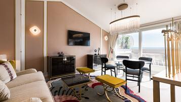 Una sala de estar moderna con sofá, mesa de centro y sillas, un televisor de pantalla plana y un ventanal con vistas al océano.