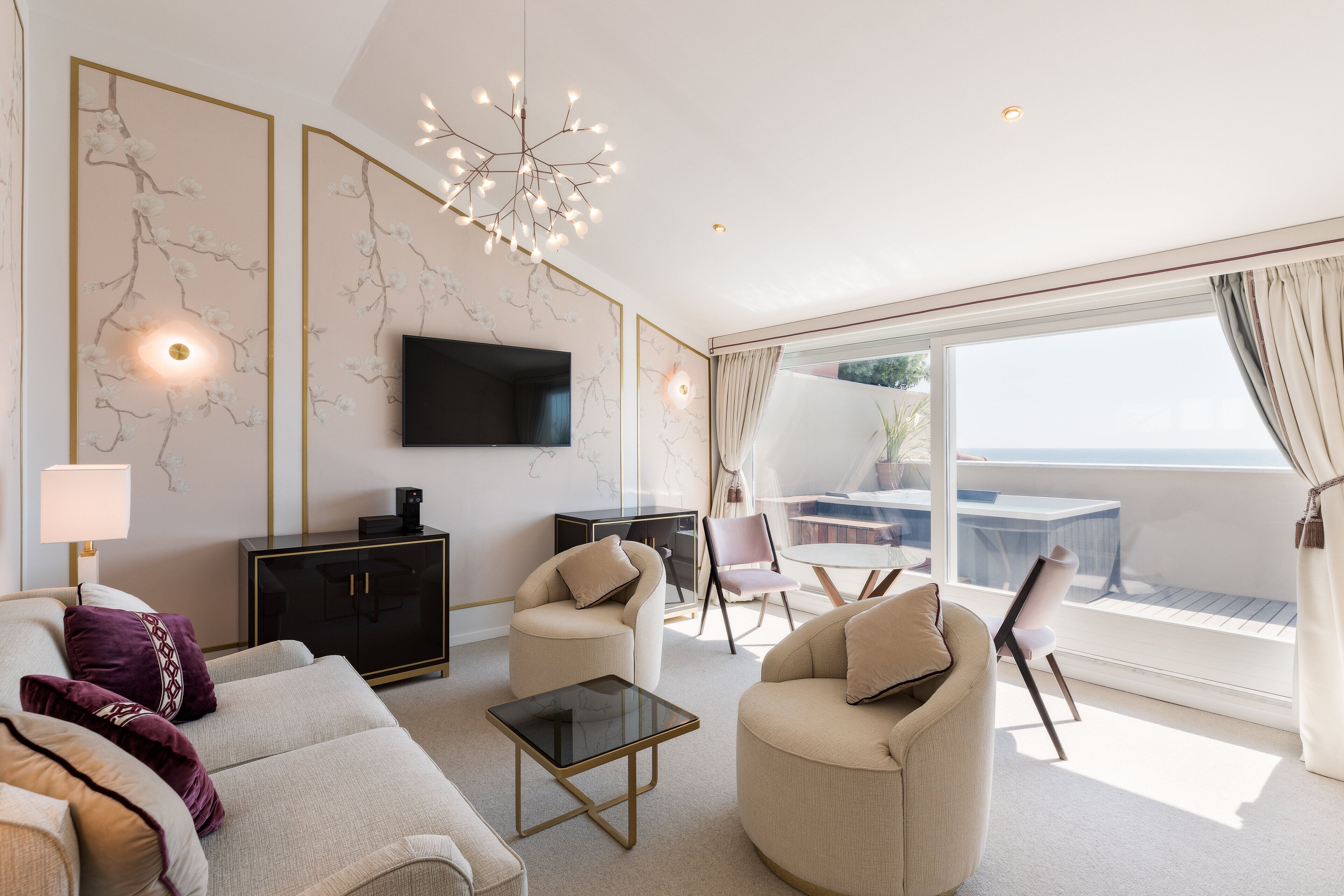 Una sala de estar moderna con sofá, sillones, una mesa de centro, televisor y un balcón con mesa y sillas.