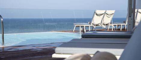 Un espace aménagé au bord de la piscine, avec des chaises longues et une vue sur l’océan.