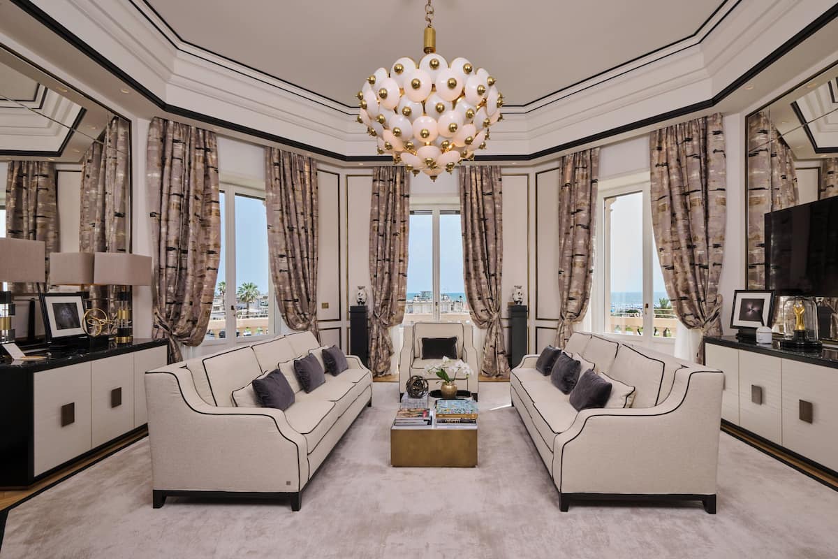 A luxurious living room with two sofas, a chandelier, and a large TV.