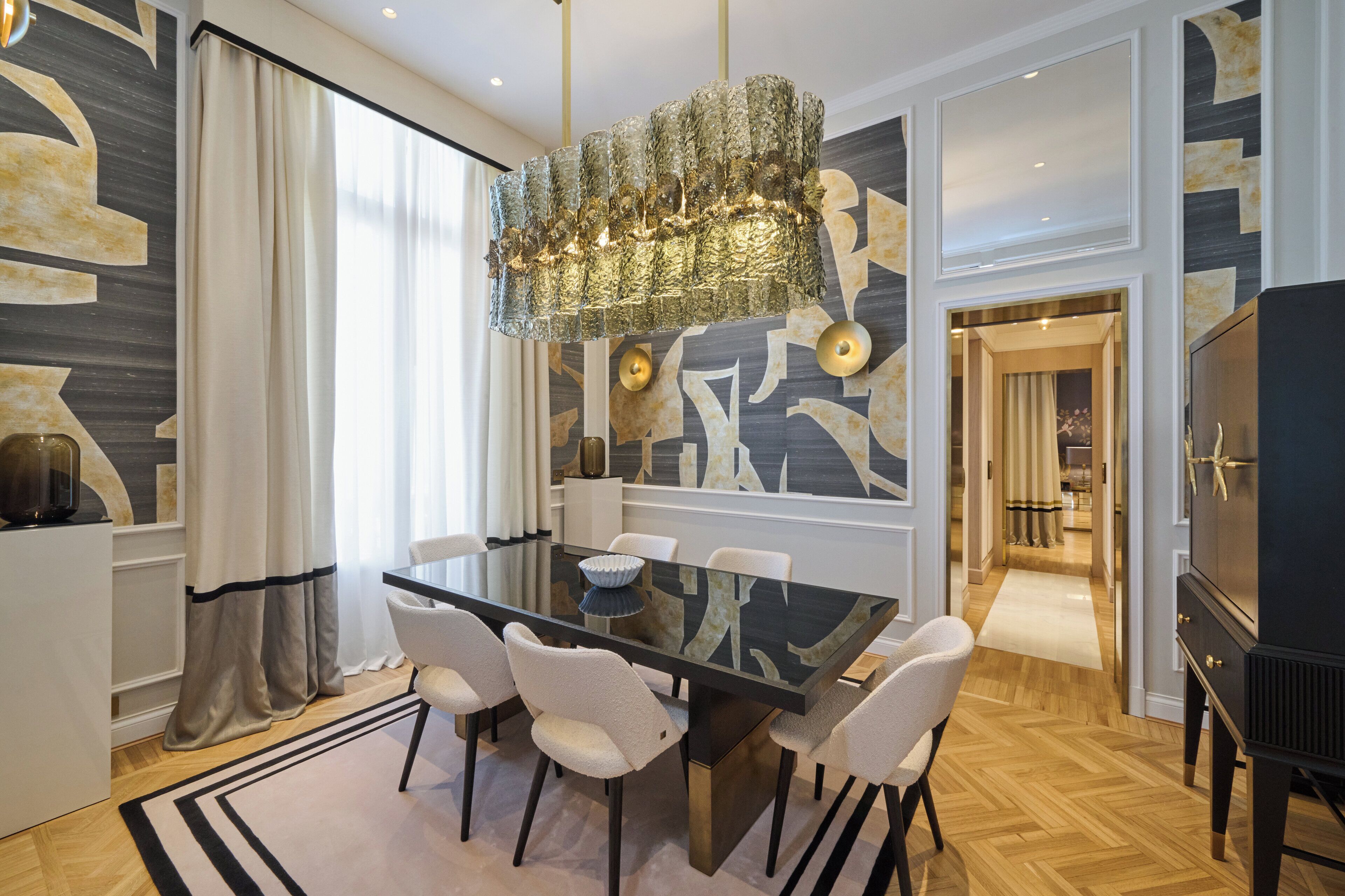 A modern dining area with a glass table, white chairs, and a decorative chandelier.