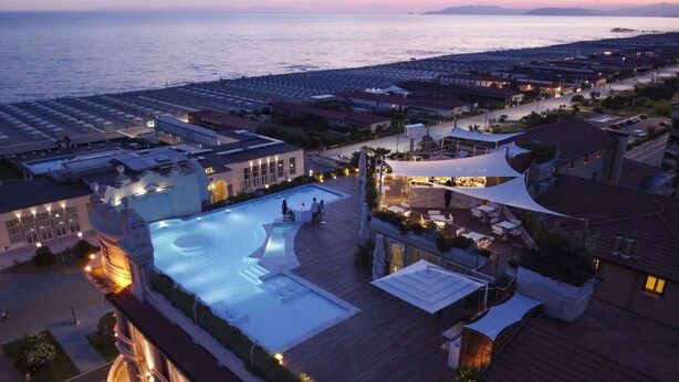A resort with a large swimming pool, outdoor seating areas, and a view of the sea.